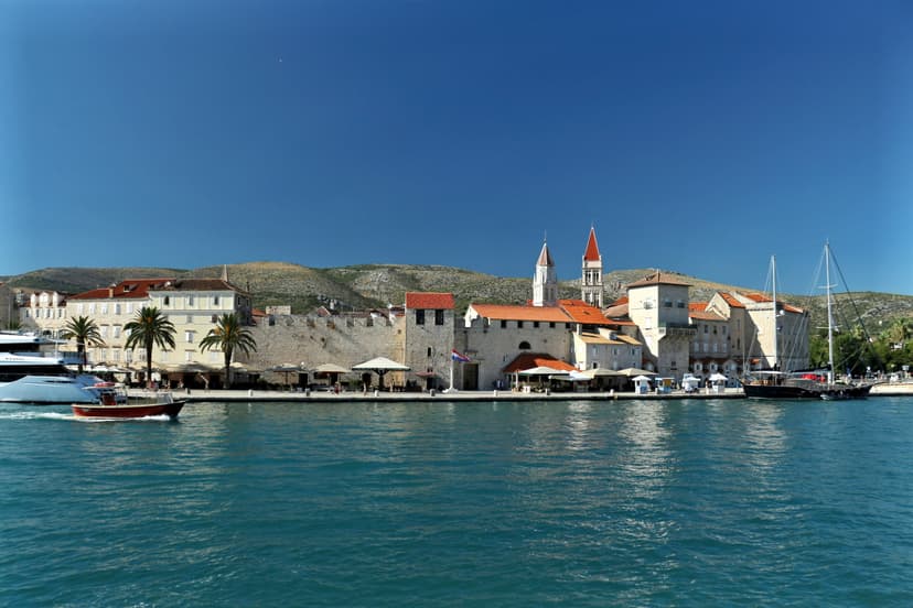 Walls, bell towers and palm trees on Trogir's waterfront seen from the channel