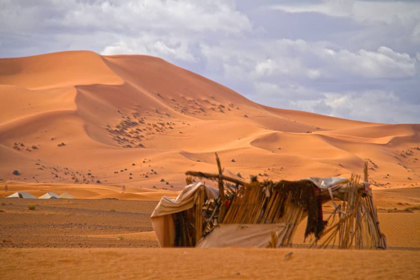 Berber shelter of branches and cloth at the foot of a tall Erg Chebbi dune, Morocco